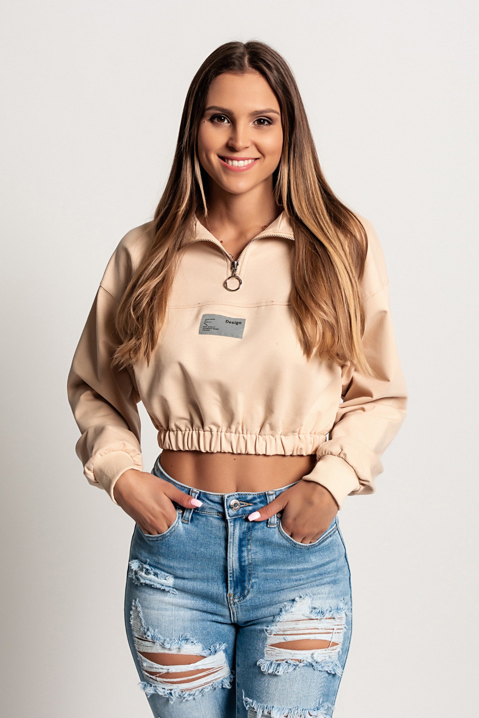 Skrajšana športna majica Polistena v bež barvi z dolgimi rokavi in visokim ovratnikom z zadrgo.